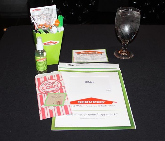 photo of servpro handbook for ethics course with goodie bag in the left corner of the phote, deodorize, and a popcorn bag