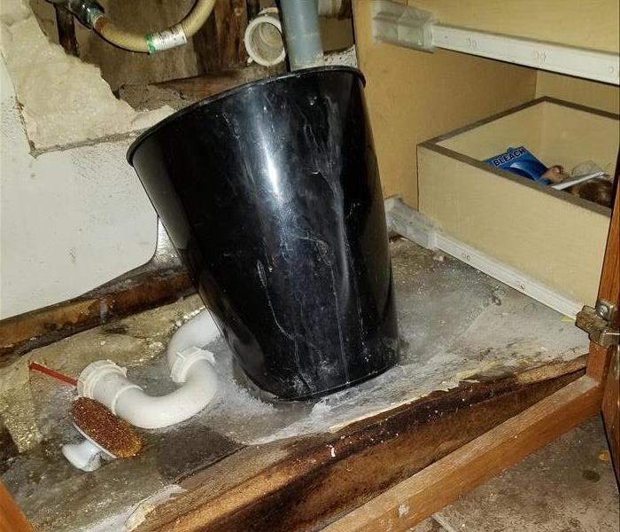 black bucket under a sink  with collapsed board and ice coming from the sink's water valve
