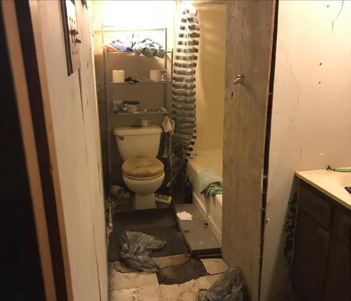 bathroom with soiled contents on the ground and shelves, part of the tile flooring ripped out 