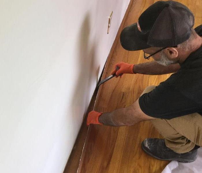 servpro employee bending down on one knee removing living room baseboard 